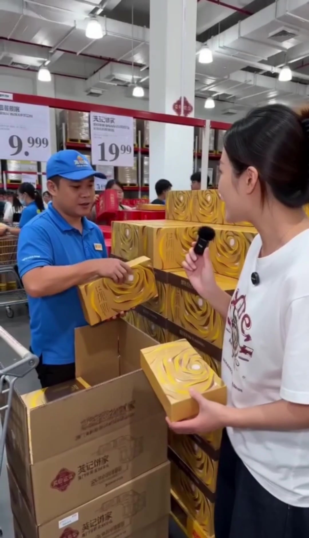 商超售货员向手持麦克风的女士介绍金色月饼礼盒