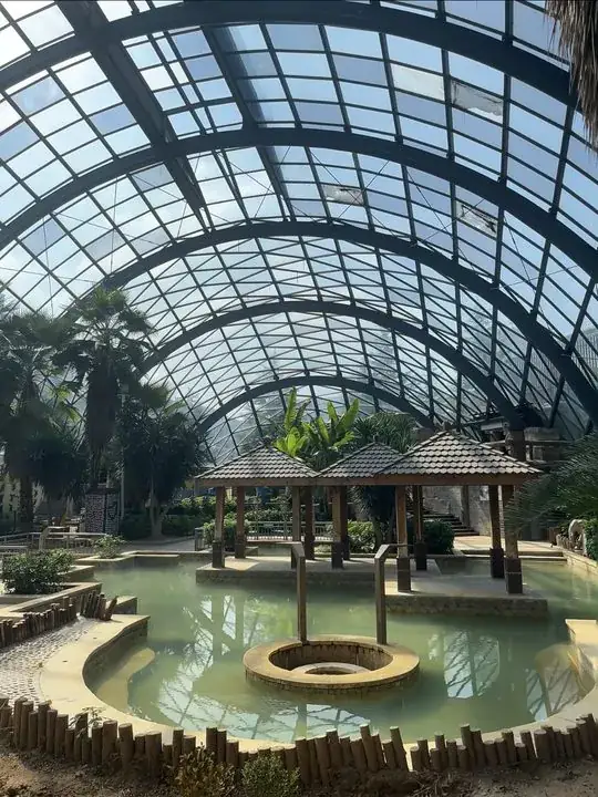 玻璃穹顶覆盖的室内温泉空间,中央设有亭台与环形泡池