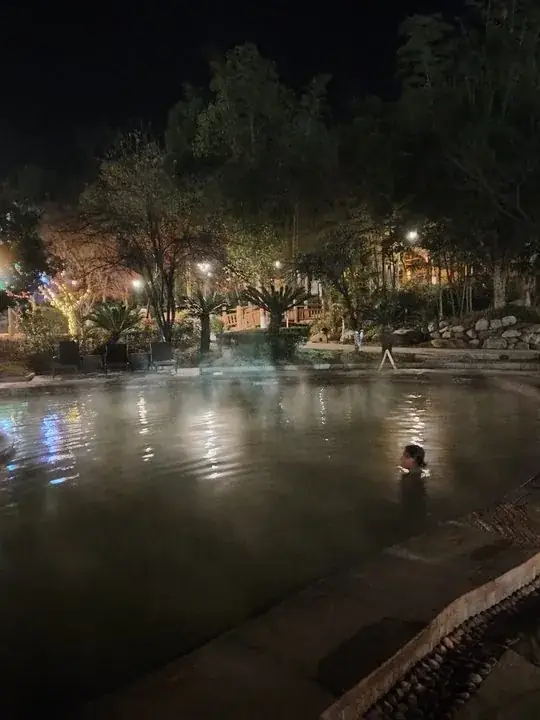 夜间露天温泉池中有一名体验者,庭院灯光倒映在水面并可见蒸汽