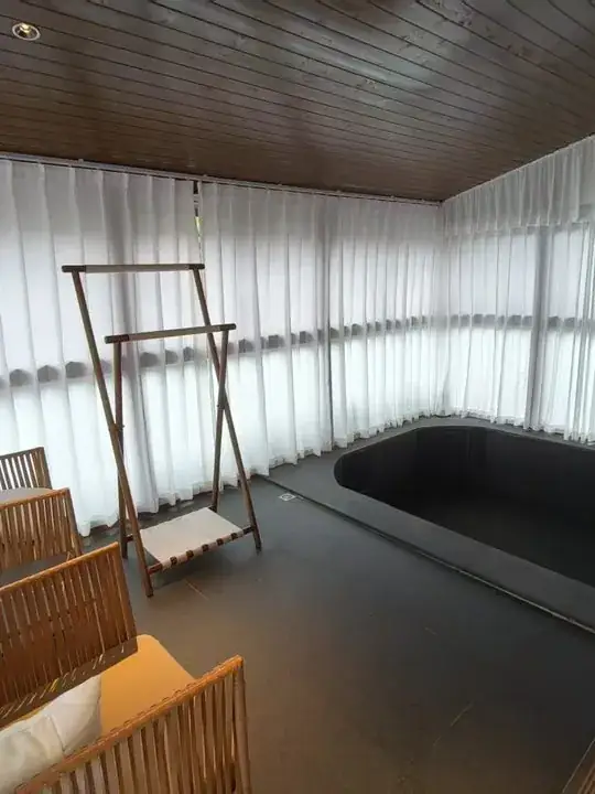 白色纱帘围合的室内休憩空间,设有深色圆形私享泡池和竹木座椅